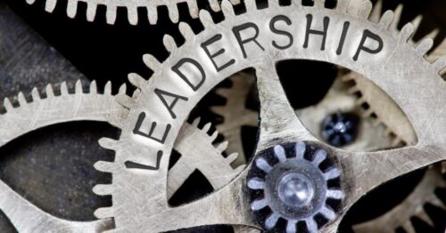 Leadership is written in large capital letters on a cog that is part of a larger mechanism