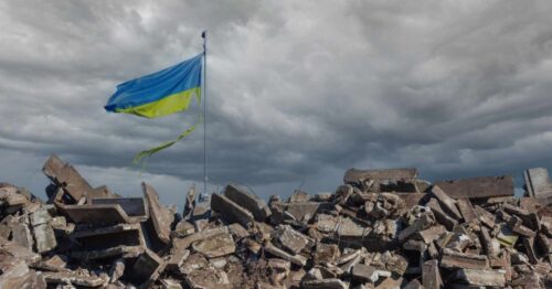 A tattered flag of Ukraine stands above a pile of rubble